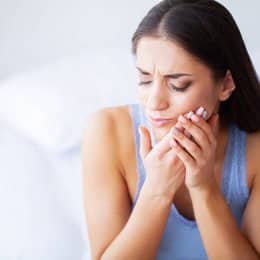 Woman holding cheek in pain, experiencing dental discomfort or toothache indoors.