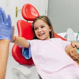 Young girl wearing boxing gloves giving high-five in dental office setting