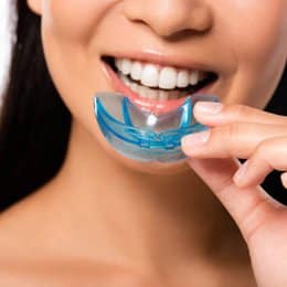 Woman smiling while inserting blue dental night guard into her mouth