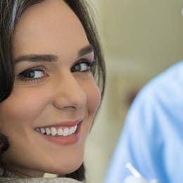 Woman smiling at dental office, displaying healthy teeth during checkup appointment.
