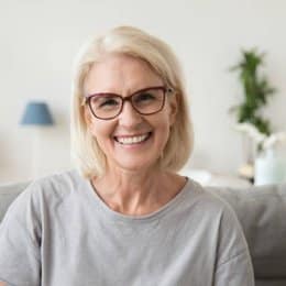 Smiling woman with blonde hair wearing glasses in modern dental office setting.