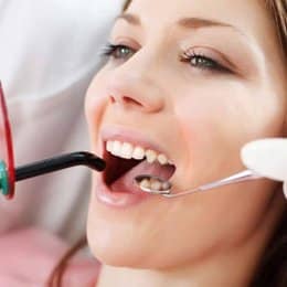 Woman undergoing dental examination with dentist using mirror and suction tools in clinical setting.