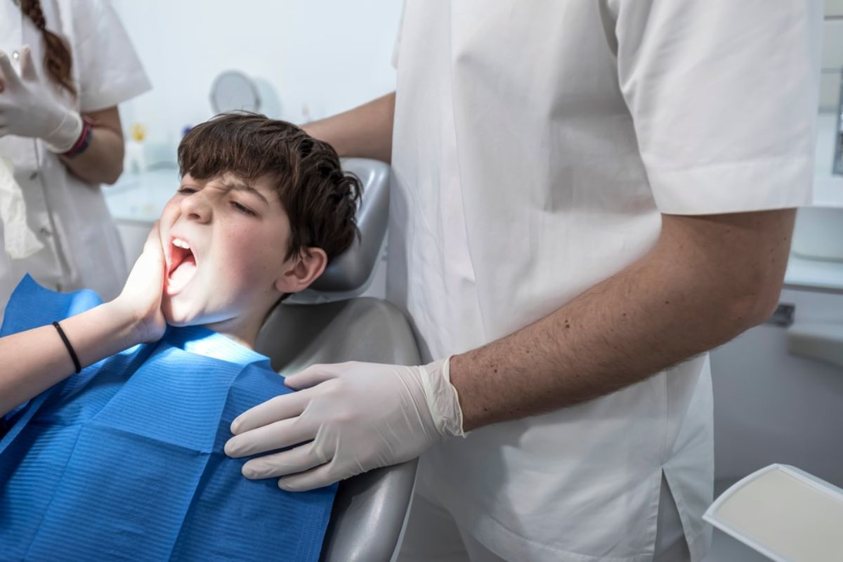 Young boy receiving dental examination from dentist in clinical setting with blue bib.