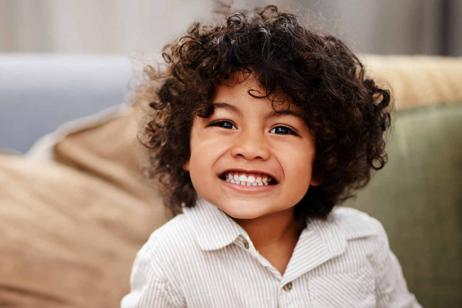 Happy young child with curly hair smiling indoors on couch